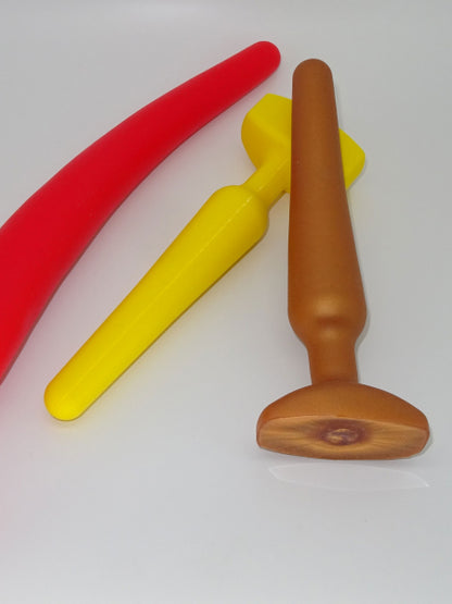 Premium silicone anal plug in "Unicorn 2" design by 1ATOYS, displayed in red, yellow, and copper for size comparison of the different variants.